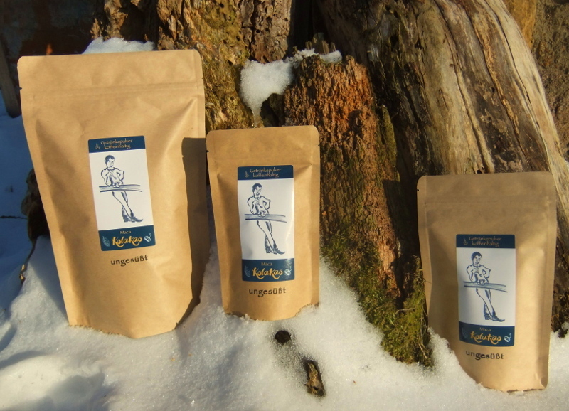 Die 3 Packungsgrößen (600g, 200g, 80g) von KolaKao Maca ungesüßt, steht auf den Scheeresten des letzten Winters, umgeben von malerisch zerfressenem Totholz im Obsthang vom Schloß Batzdorf.